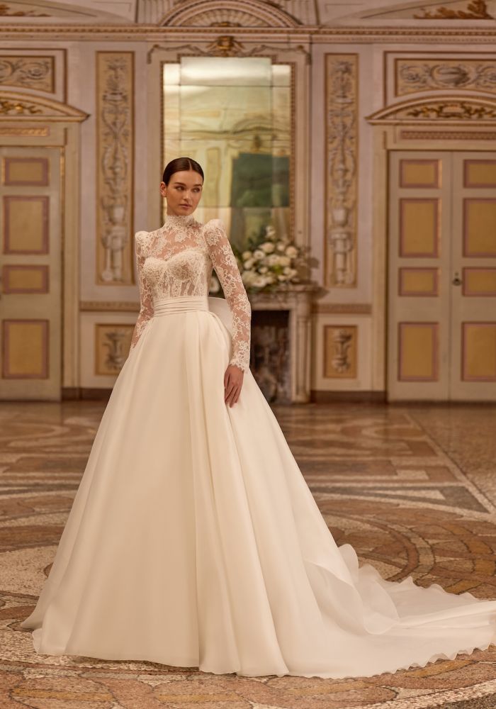 Robe de mariée ARTEMISIA de  – Matière : dentelle – dentelle, satin, organza, boléro amovible dentelle, col montant manches longues, traîne amovible, cérémonie religieuse
